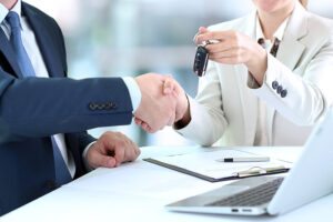 Two people shaking hands over a table with keys.